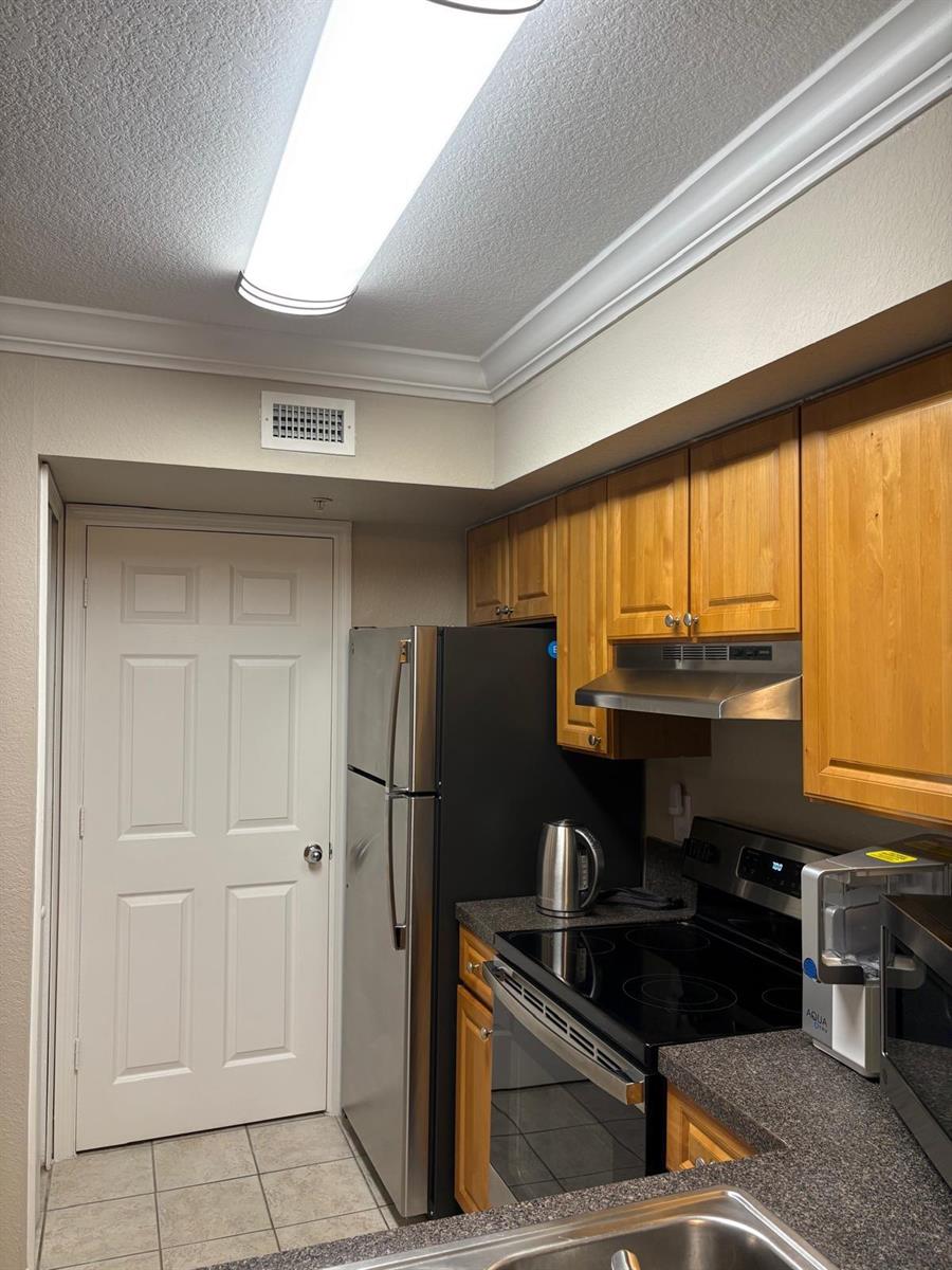 A kitchen features wood cabinets, stainless steel appliances, and a gray countertop — 15075 Michelangelo Boulevard # 204, Delray Beach FL 33446, DELRAY BEACH, FL