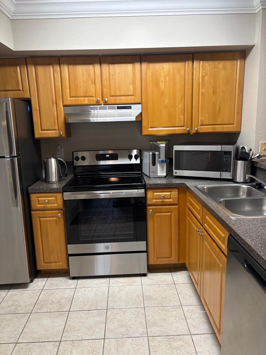 A kitchen features wood cabinets, stainless steel appliances, dark countertops, and light-colored floor tiles — 15075 Michelangelo Boulevard # 204, Delray Beach FL 33446, DELRAY BEACH, FL