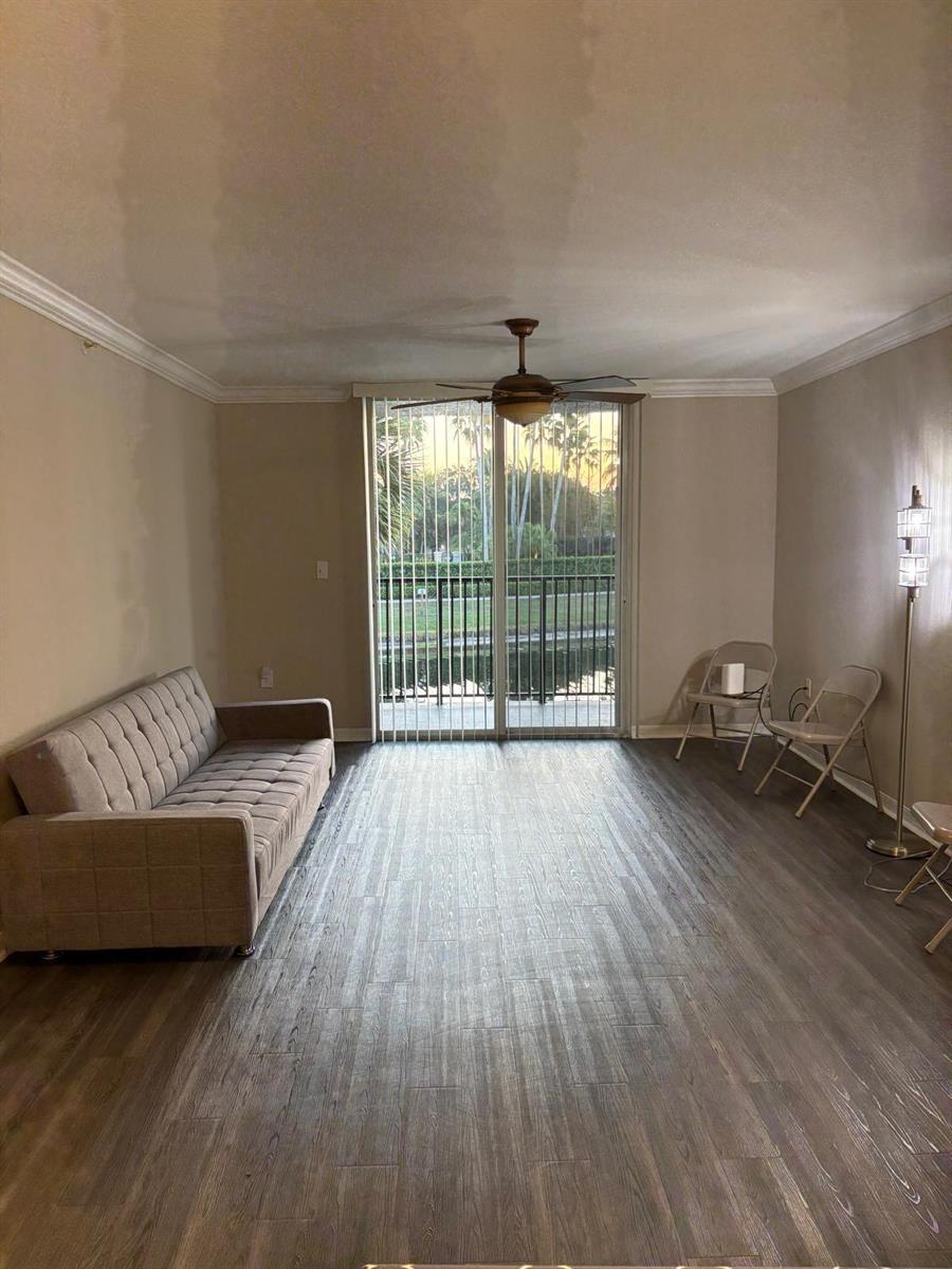 A living room with wood-look flooring, a beige sofa, folding chairs, and a sliding glass door — 15075 Michelangelo Boulevard # 204, Delray Beach FL 33446, DELRAY BEACH, FL
