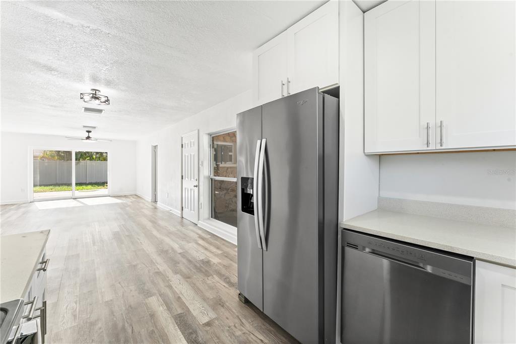 A kitchen with white cabinets and stainless steel appliances opens into a living area — 6221 FLORIDA CIRCLE E, APOLLO BEACH, FL