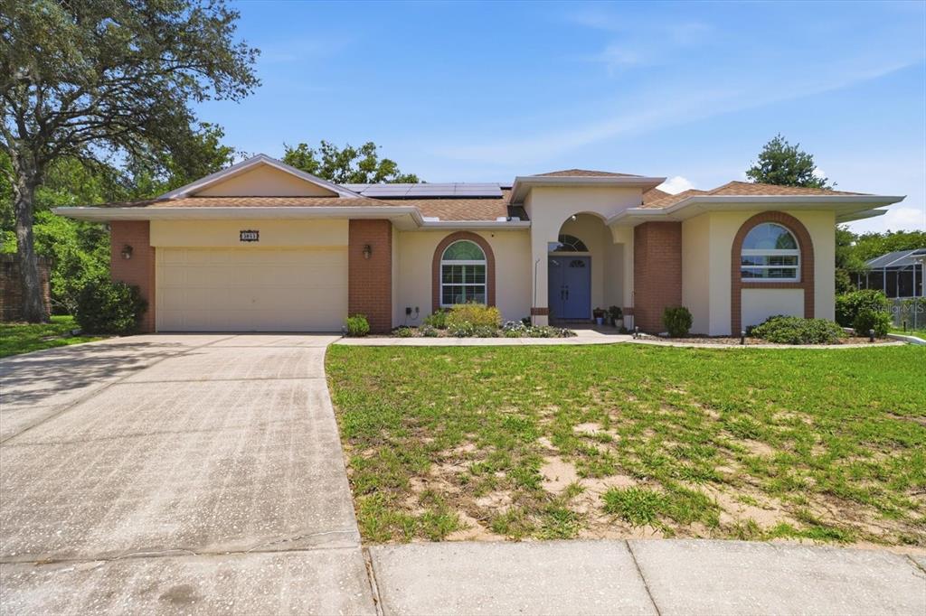 A single-story house with a two-car garage, brick accents, and solar panels on the roof — 3843 W NORTHCREST COURT, LECANTO, FL