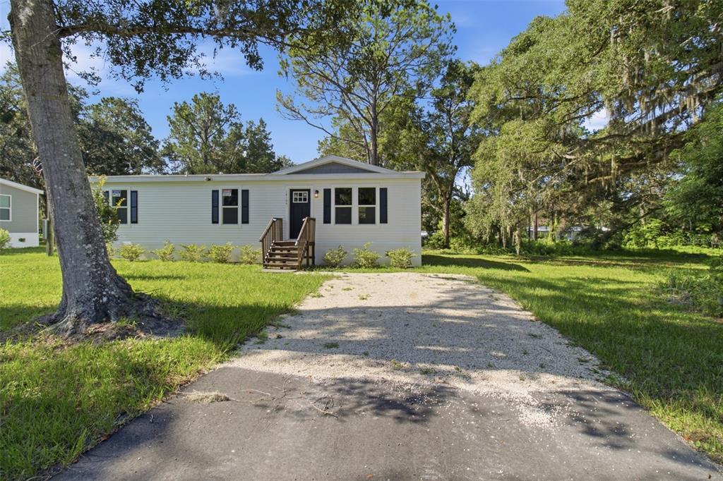 A single-story manufactured home with a gravel driveway and wooden front steps — 18104 NICHOLAS AVENUE, BROOKSVILLE, FL