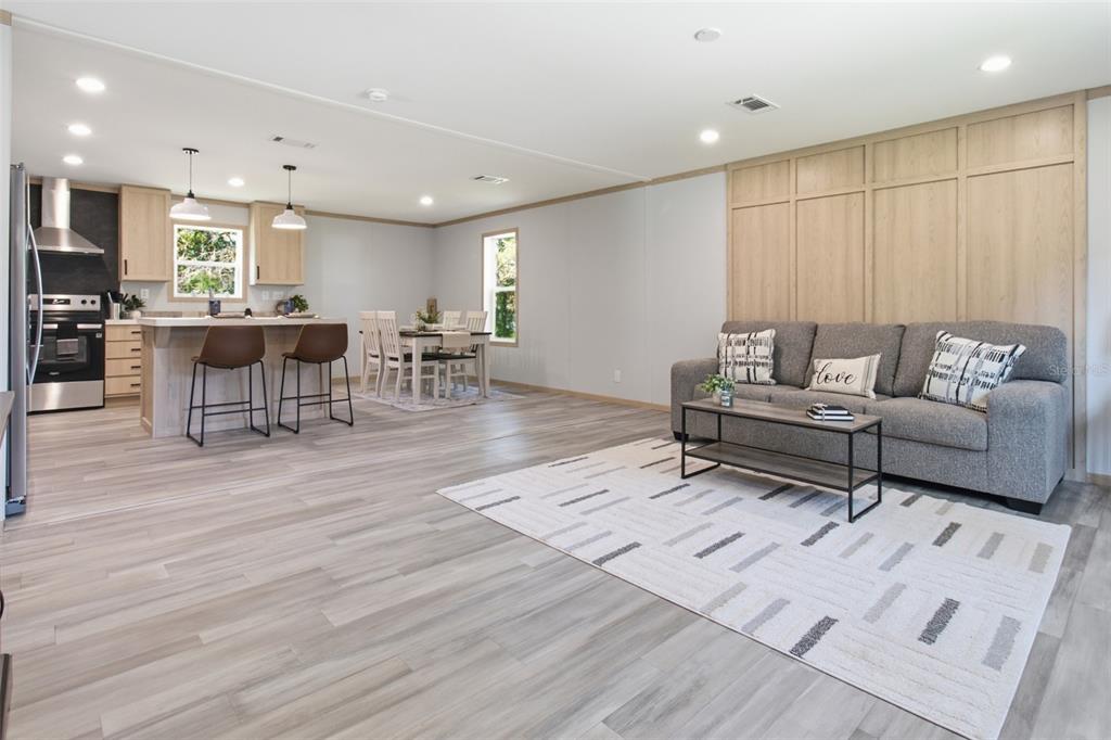 An open-concept living and dining area features light wood flooring, a gray sofa, and cabinetry — 18104 NICHOLAS AVENUE, BROOKSVILLE, FL