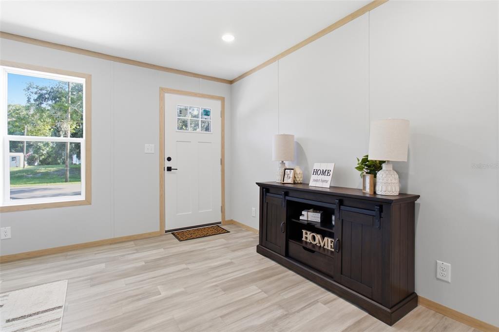 A bright room features light wood-look flooring, a white front door, and a dark console table — 18104 NICHOLAS AVENUE, BROOKSVILLE, FL