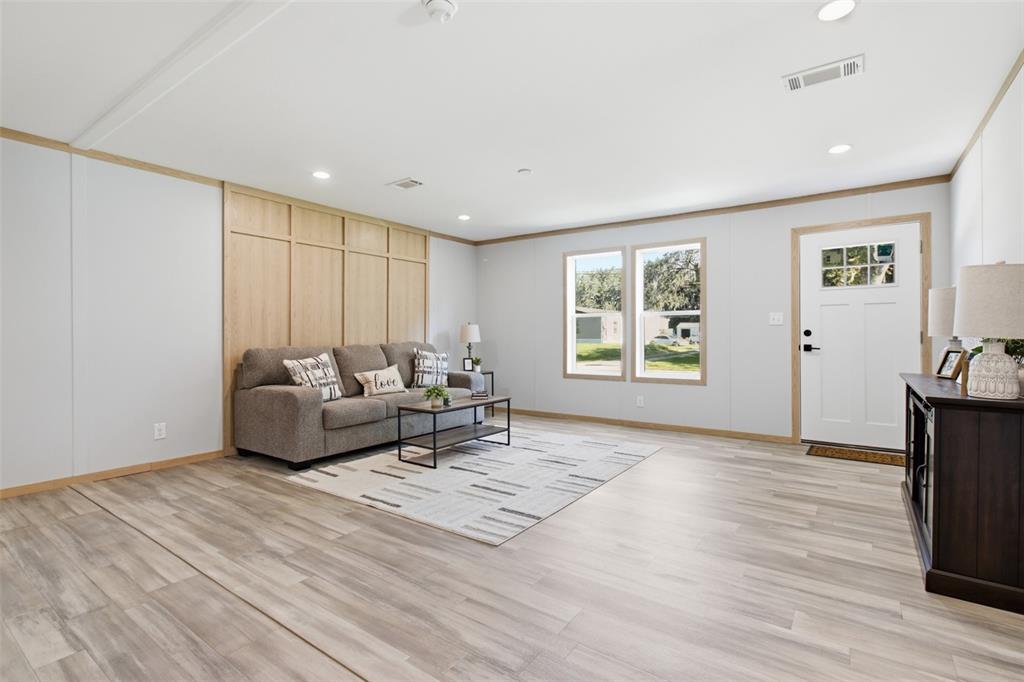 A living room features light wood-look flooring, a paneled accent wall, and a gray sofa — 18104 NICHOLAS AVENUE, BROOKSVILLE, FL