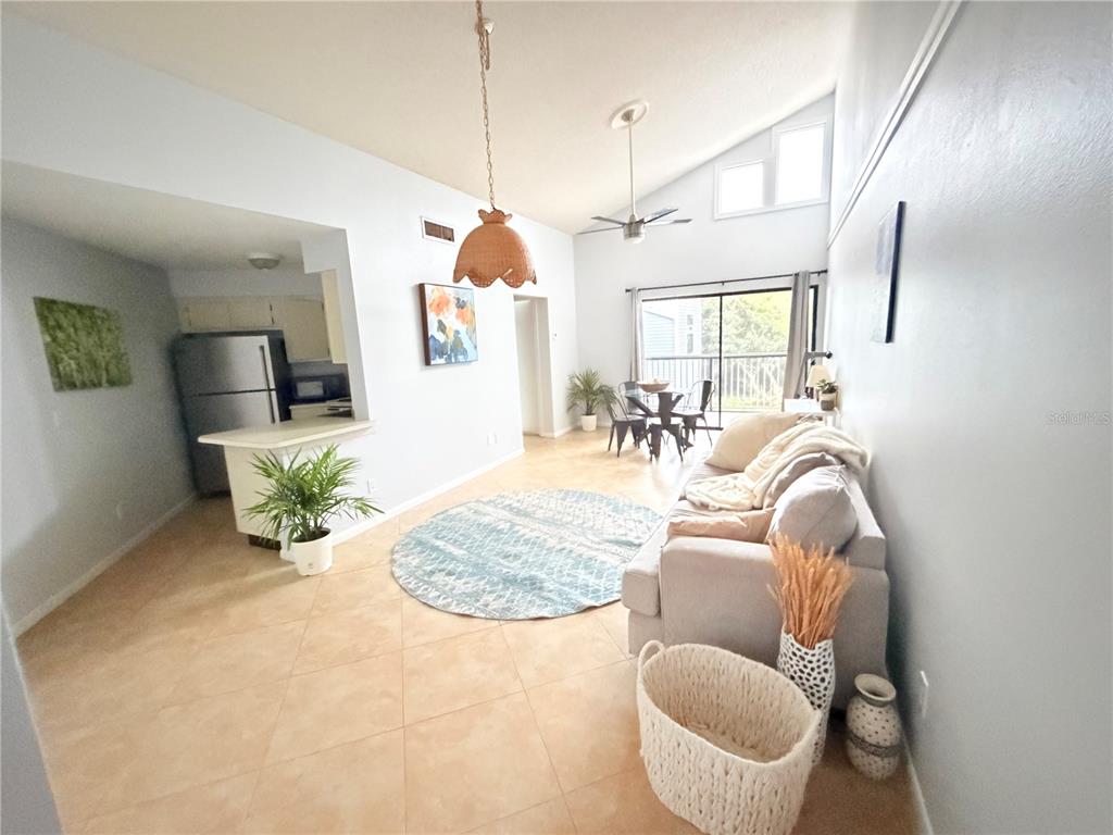 A living room with vaulted ceilings, tile floors, a sofa, and an open kitchen area — 3914 ATRIUM DRIVE UNIT U1, ORLANDO, FL