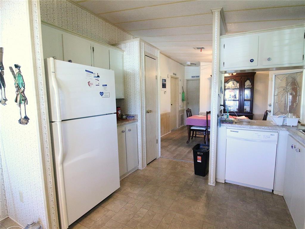 A kitchen with white appliances, light-colored cabinets, and vinyl flooring leads into a dining area — 145 JANA CIRCLE, AUBURNDALE, FL