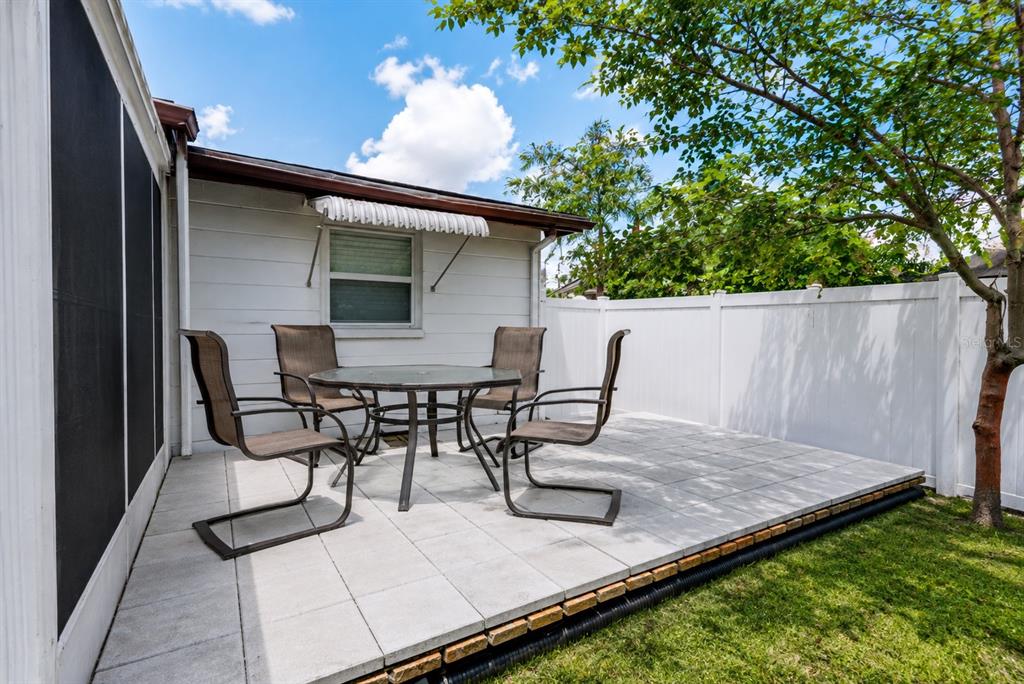 A patio with a glass-topped table and four chairs sits against a white house exterior — 3302 ROCK ROYAL DRIVE, HOLIDAY, FL