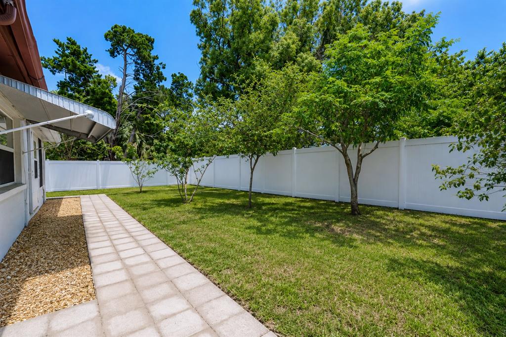 A backyard features a paved walkway, a white vinyl fence, and several small trees — 3302 ROCK ROYAL DRIVE, HOLIDAY, FL
