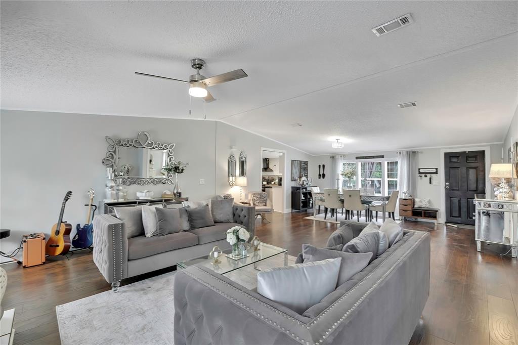 A spacious living room features gray tufted sofas, hardwood floors, and an open dining area — 6171 S LISA POINT, HOMOSASSA, FL