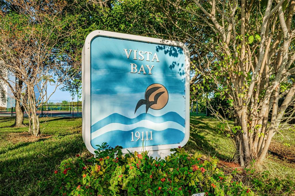 A sign for Vista Bay stands in a grassy area surrounded by trees and bushes — 19111 VISTA BAY DRIVE UNIT 304, INDIAN SHORES, FL