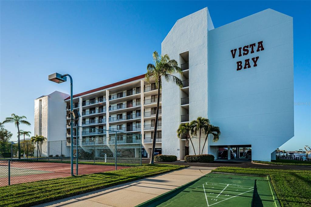The exterior of the white Vista Bay apartment building features a tennis court and shuffleboard court — 19111 VISTA BAY DRIVE UNIT 304, INDIAN SHORES, FL