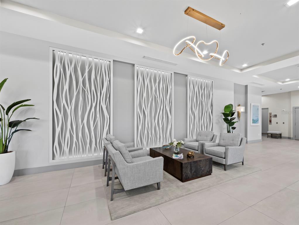 A modern lobby features gray armchairs, a dark coffee table, and decorative white wall panels — 3080 GRAND BAY BOULEVARD UNIT 512, LONGBOAT KEY, FL