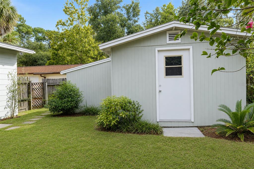 A light green shed with a white door sits in a grassy backyard — 703 NE 6TH PLACE, GAINESVILLE, FL