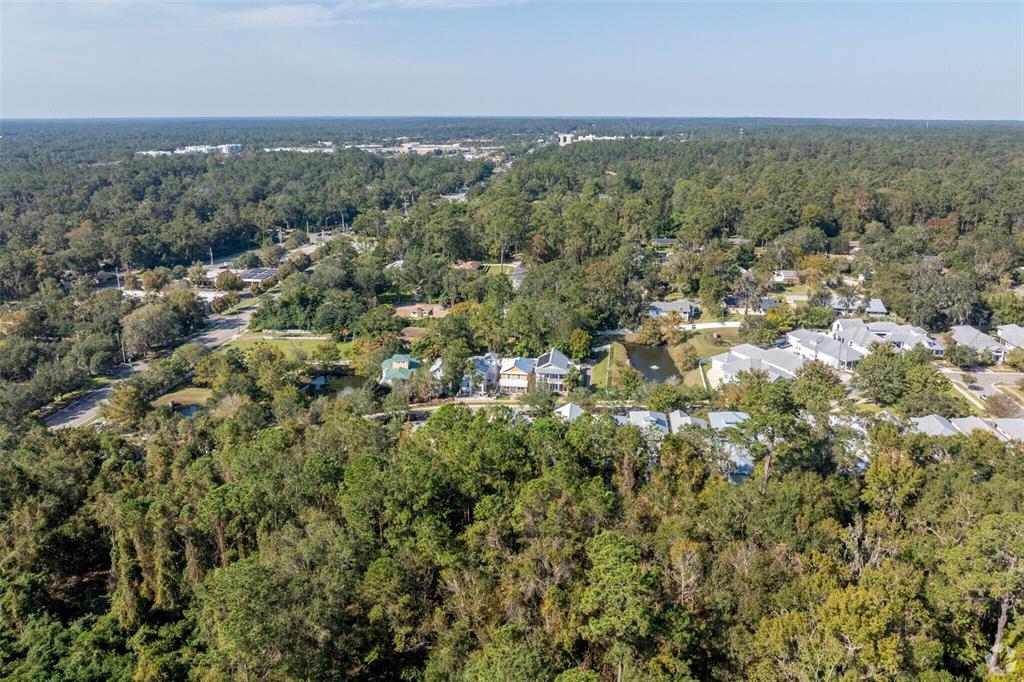 An aerial view shows a residential neighborhood surrounded by dense forest under a clear sky — 703 NE 6TH PLACE, GAINESVILLE, FL