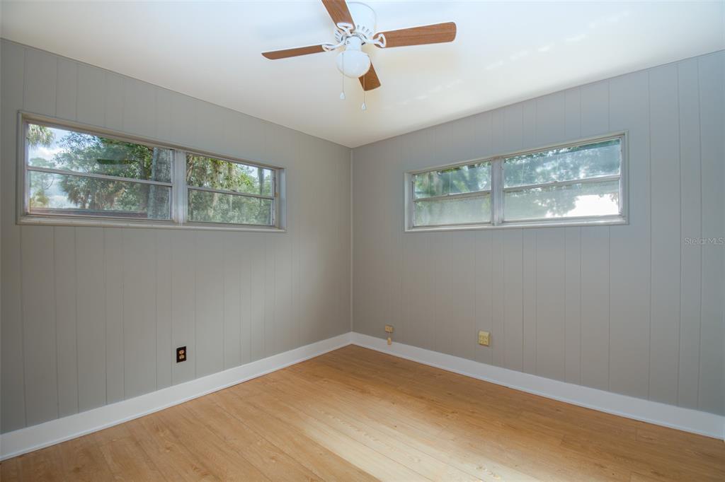 An empty bedroom features light gray paneled walls, wood-look flooring, and a ceiling fan — 703 NE 6TH PLACE, GAINESVILLE, FL