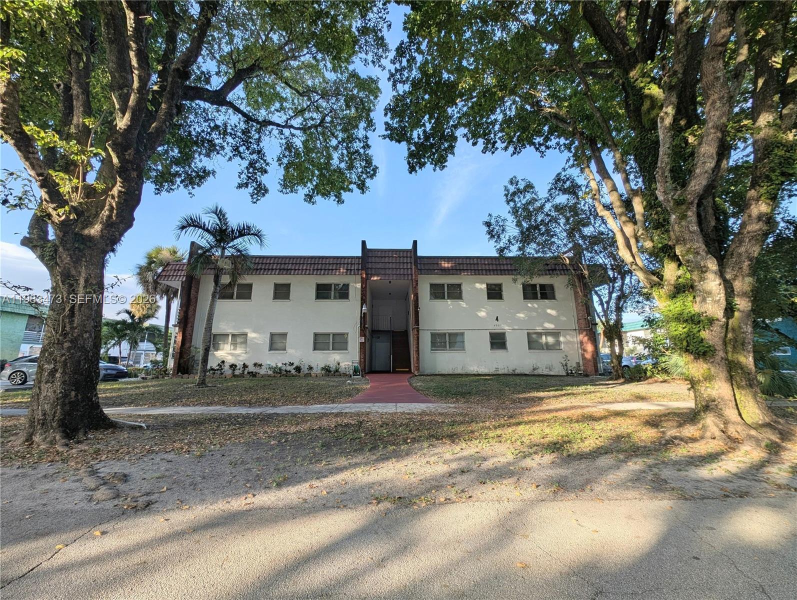 A two-story apartment building with a central entrance is framed by large, mature trees — 4801 NW 22nd Ct # 205, Lauderhill FL 33313, LAUDERHILL, FL