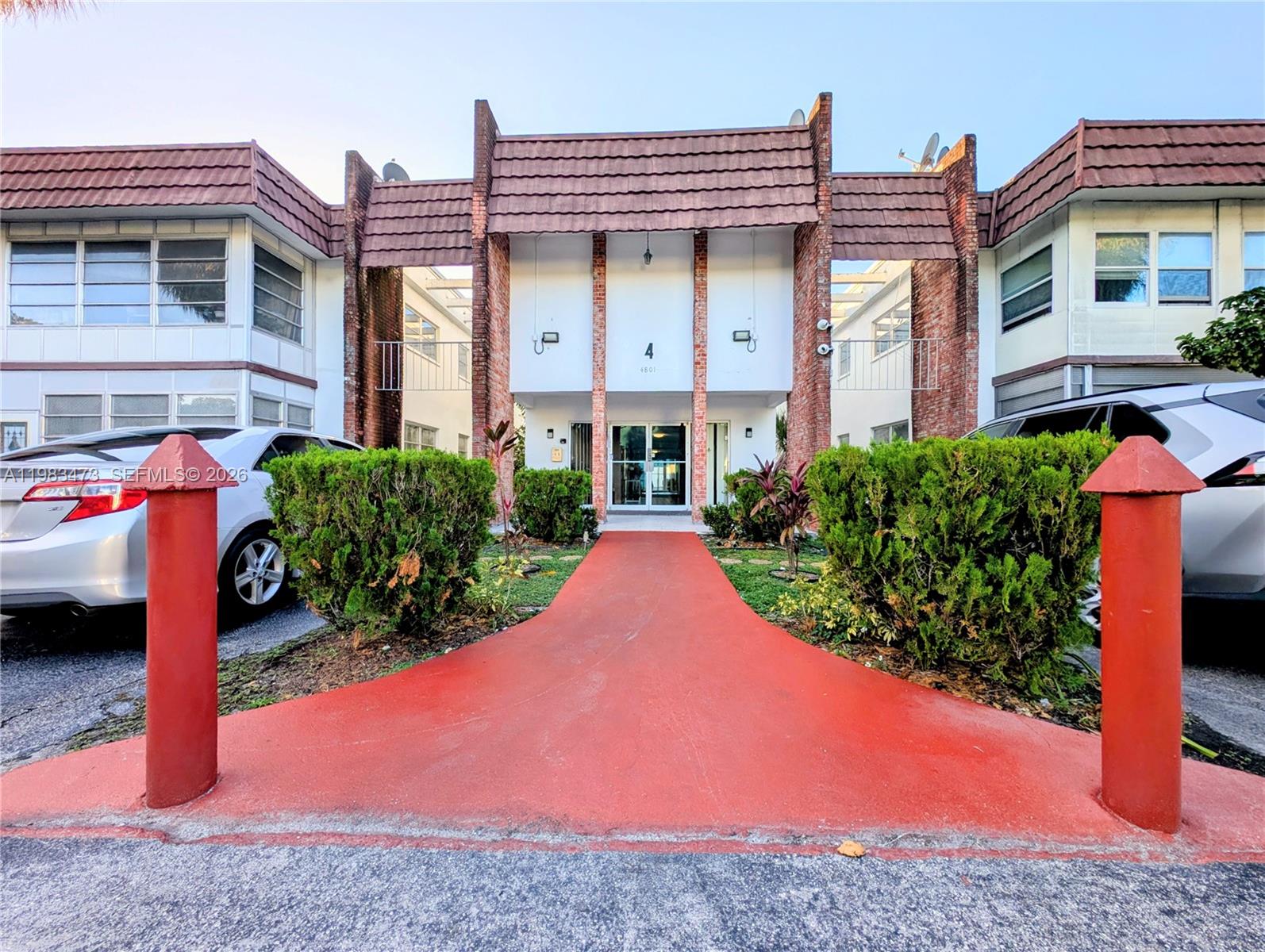 A red walkway leads to the entrance of a two-story apartment building with brick accents — 4801 NW 22nd Ct # 205, Lauderhill FL 33313, LAUDERHILL, FL