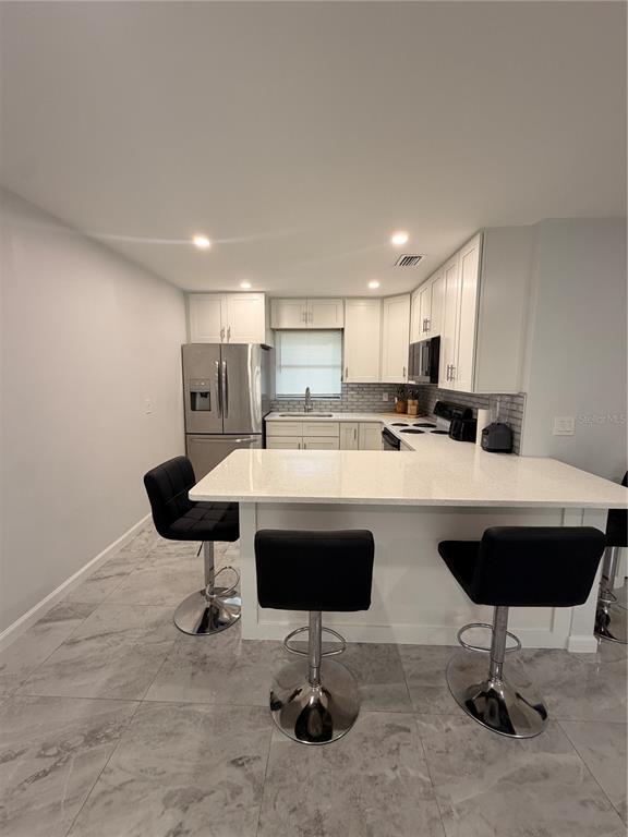 A kitchen features white cabinets, stainless steel appliances, a quartz island, and gray tile flooring — 1144 36TH STREET W, BRADENTON, FL