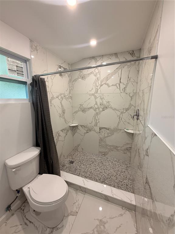 A bathroom features a walk-in shower with marble-look tile, a pebble floor, and a toilet — 1144 36TH STREET W, BRADENTON, FL
