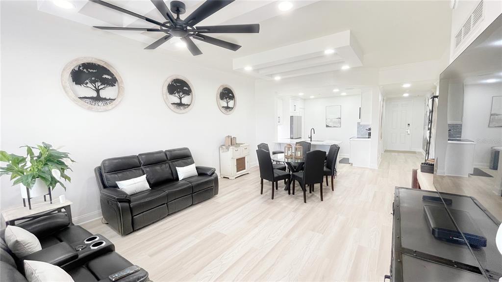 A modern open-concept living and dining area features white walls, light flooring, and black furniture — 1501 NORTHERN HARRIER WAY UNIT 202, REUNION, FL