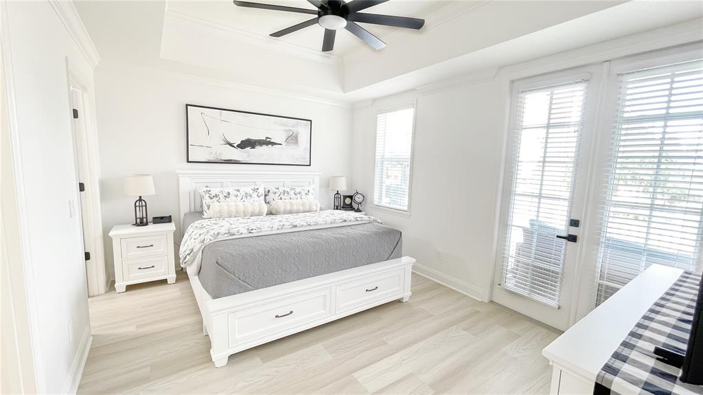 A bright bedroom features a white bed with storage drawers, light wood flooring, and French doors — 1501 NORTHERN HARRIER WAY UNIT 202, REUNION, FL