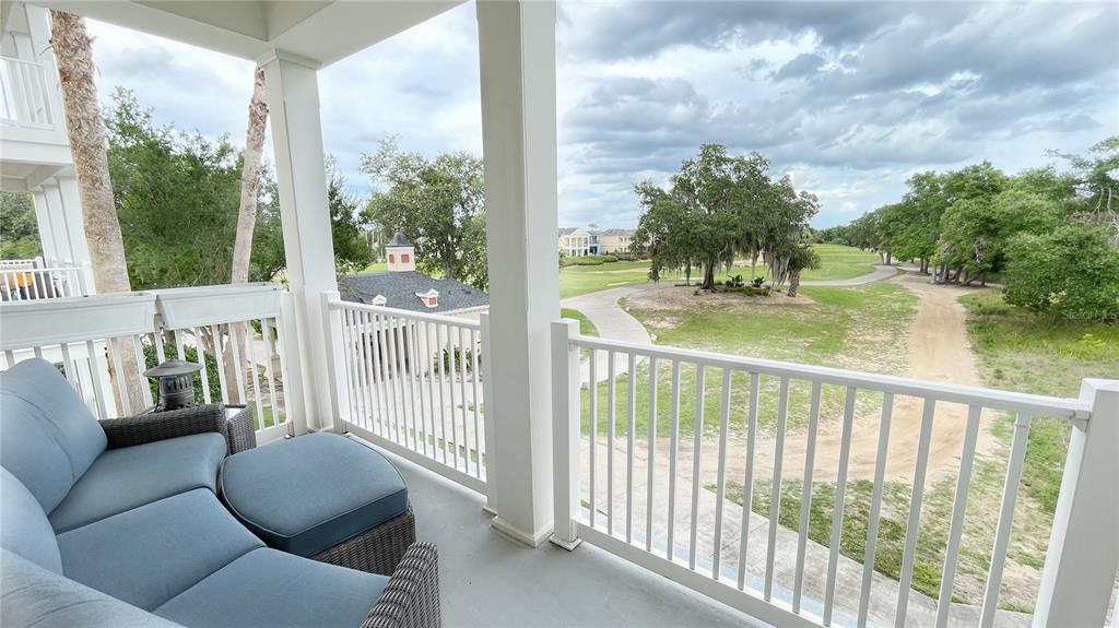 A covered balcony features blue outdoor furniture overlooking a golf course and trees — 1501 NORTHERN HARRIER WAY UNIT 202, REUNION, FL