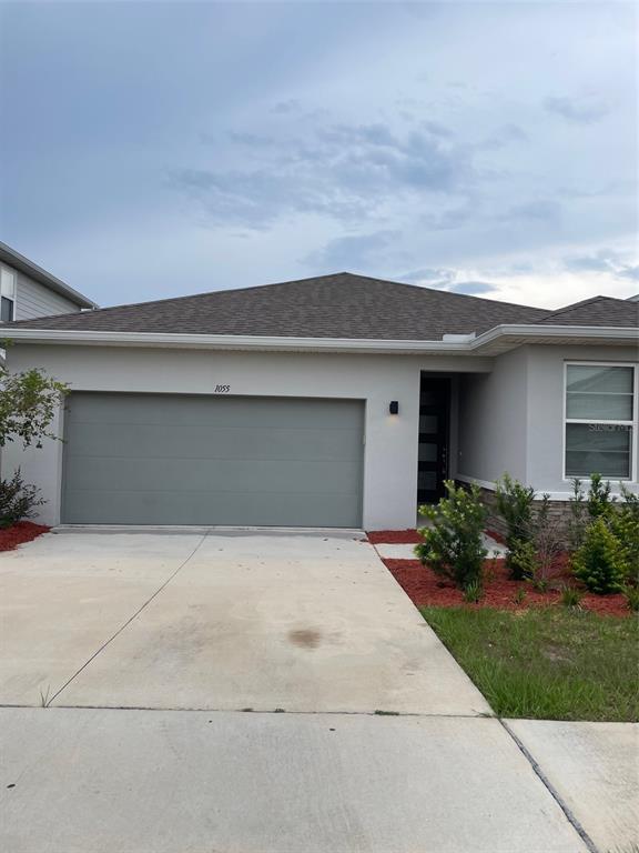 A single-story house with a gray garage door, light-colored stucco siding, and a concrete driveway — 1055 SUGARWOOD STREET, DAVENPORT, FL