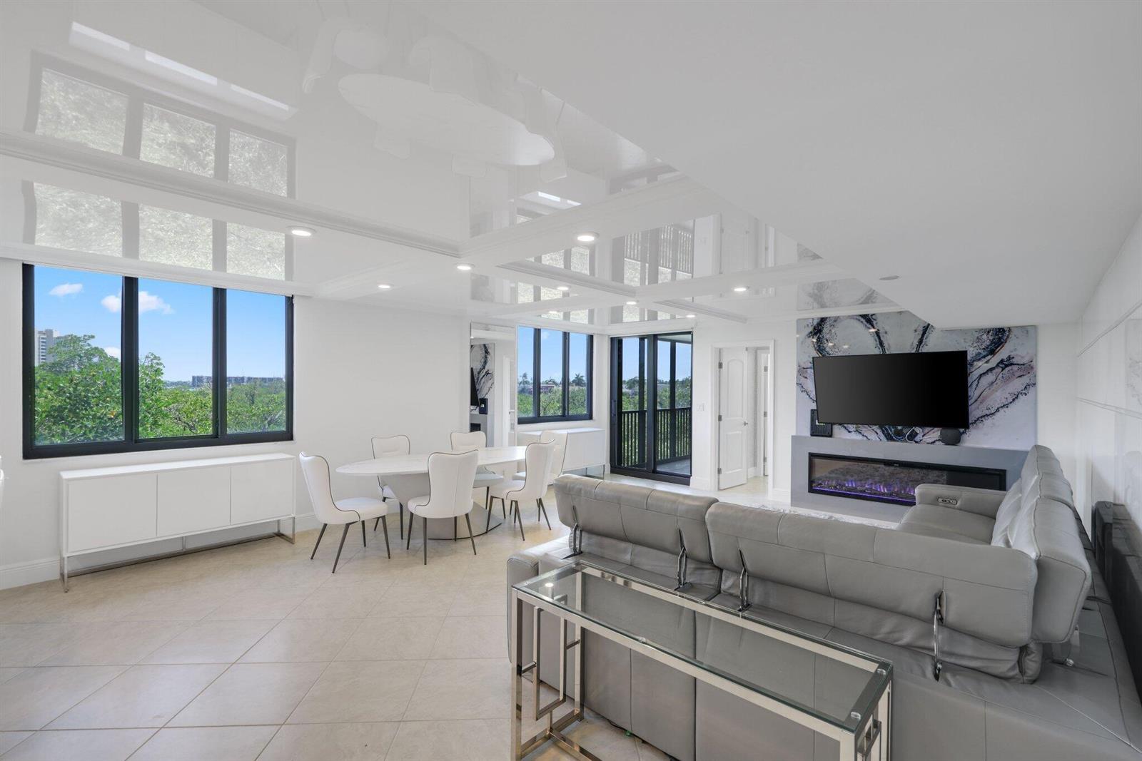 A modern living and dining area features a glossy white ceiling, fireplace, and gray sofa — 3420 S Ocean Boulevard # 4z, Highland Beach FL 33487, HIGHLAND BEACH, FL