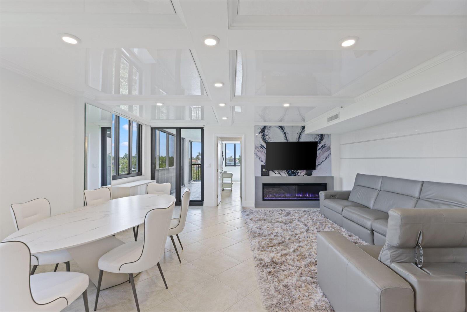 A modern living and dining area features a glossy white ceiling, fireplace, and gray sofa — 3420 S Ocean Boulevard # 4z, Highland Beach FL 33487, HIGHLAND BEACH, FL