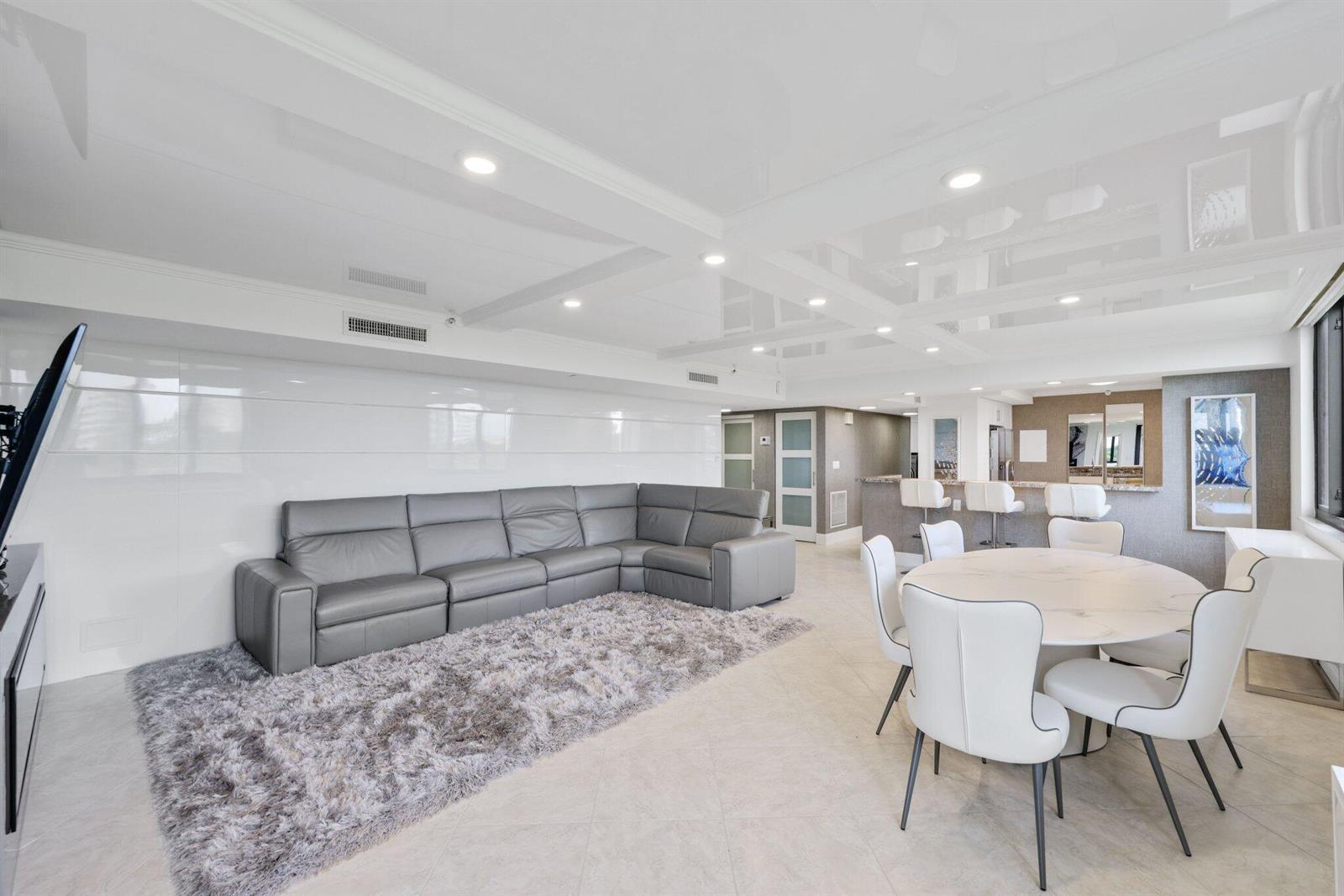 A modern open-concept living and dining area features a gray sectional, white chairs, and glossy ceilings — 3420 S Ocean Boulevard # 4z, Highland Beach FL 33487, HIGHLAND BEACH, FL