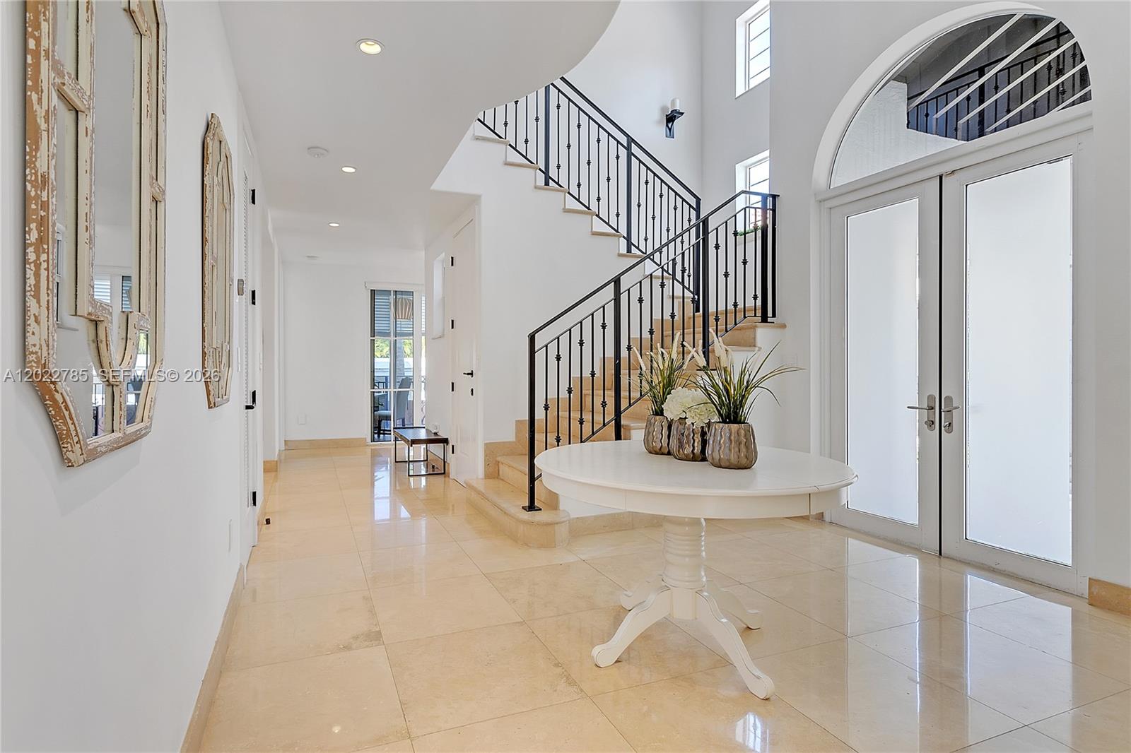 A bright foyer features a white pedestal table, a staircase with iron railings, and tile flooring — 350 Redwood Ln, Key Biscayne FL 33149, KEY BISCAYNE, FL