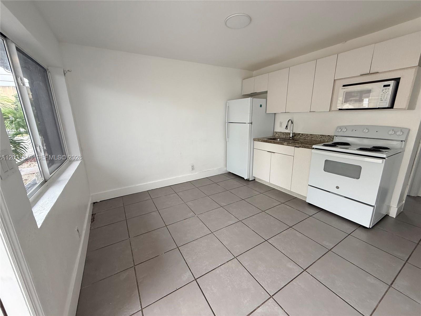 A kitchen features white cabinets, a white stove, a refrigerator, and gray tile flooring — 7824 NW 5th Ct # 7, Miami FL 33150, MIAMI, FL