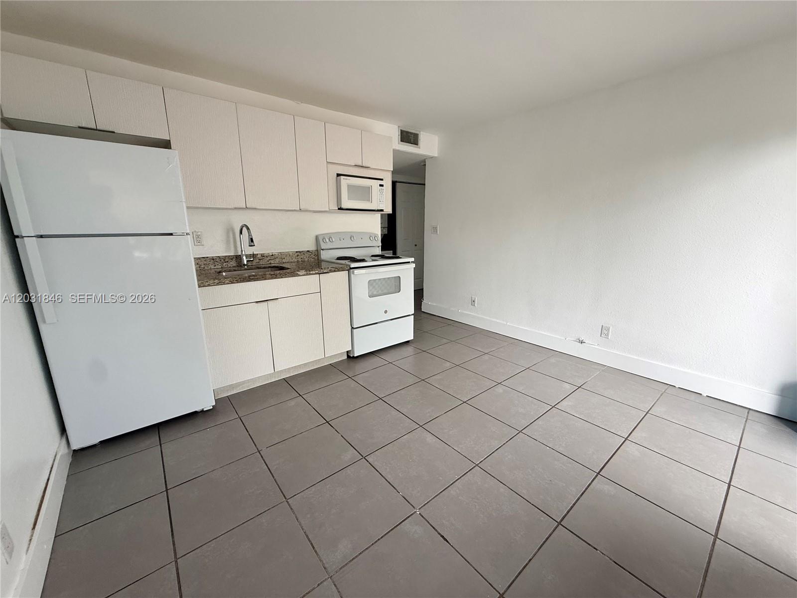 A kitchen features white cabinets, white appliances, a granite countertop, and gray tile flooring — 7824 NW 5th Ct # 7, Miami FL 33150, MIAMI, FL