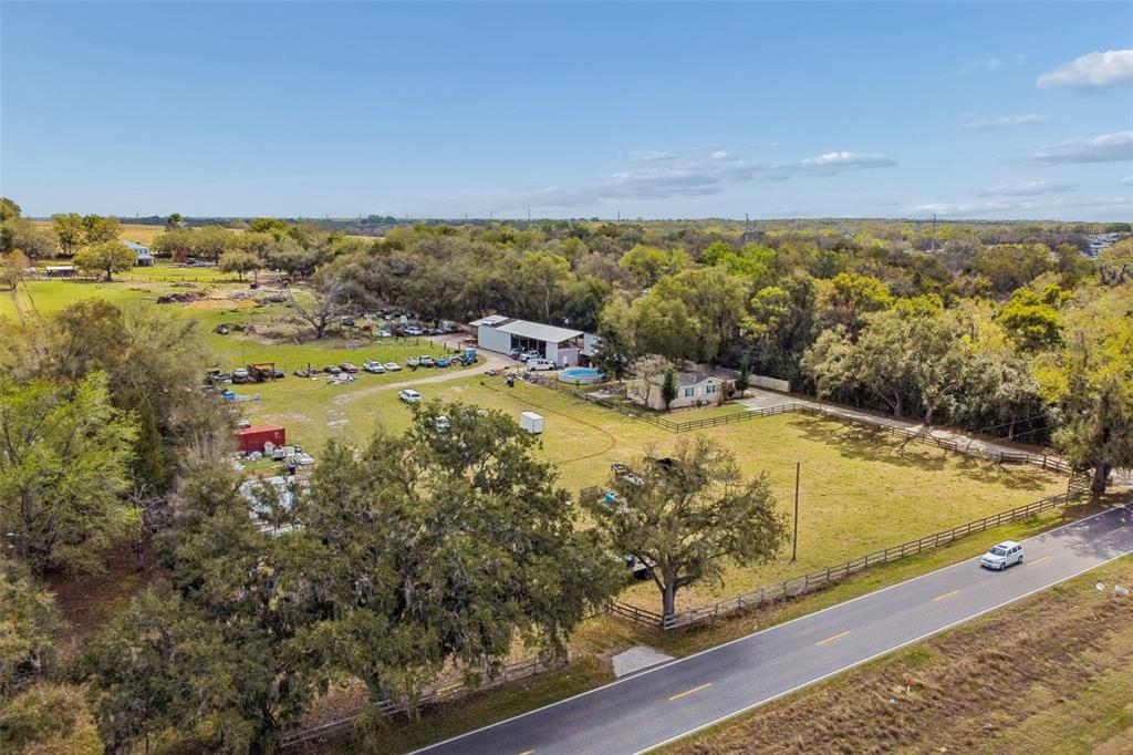 An aerial view shows a rural property with a house, a large workshop, and vehicles — 8236 WIRE ROAD, ZEPHYRHILLS, FL