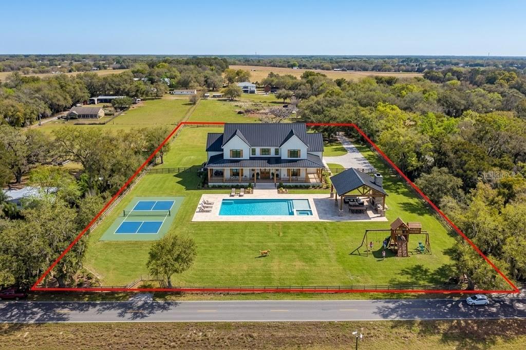 An aerial view of a white farmhouse with a pool, tennis court, and playground — 8236 WIRE ROAD, ZEPHYRHILLS, FL