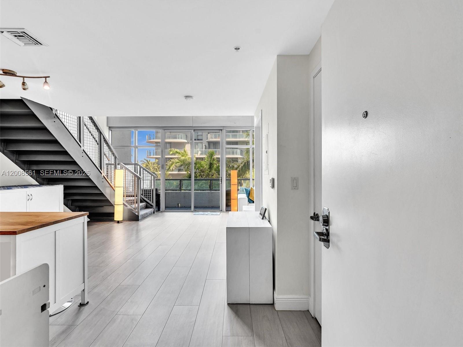 An interior view shows a living area with light wood floors, a staircase, and balcony doors — 3301 NE 1st Ave # M0306, Miami FL 33137, MIAMI, FL