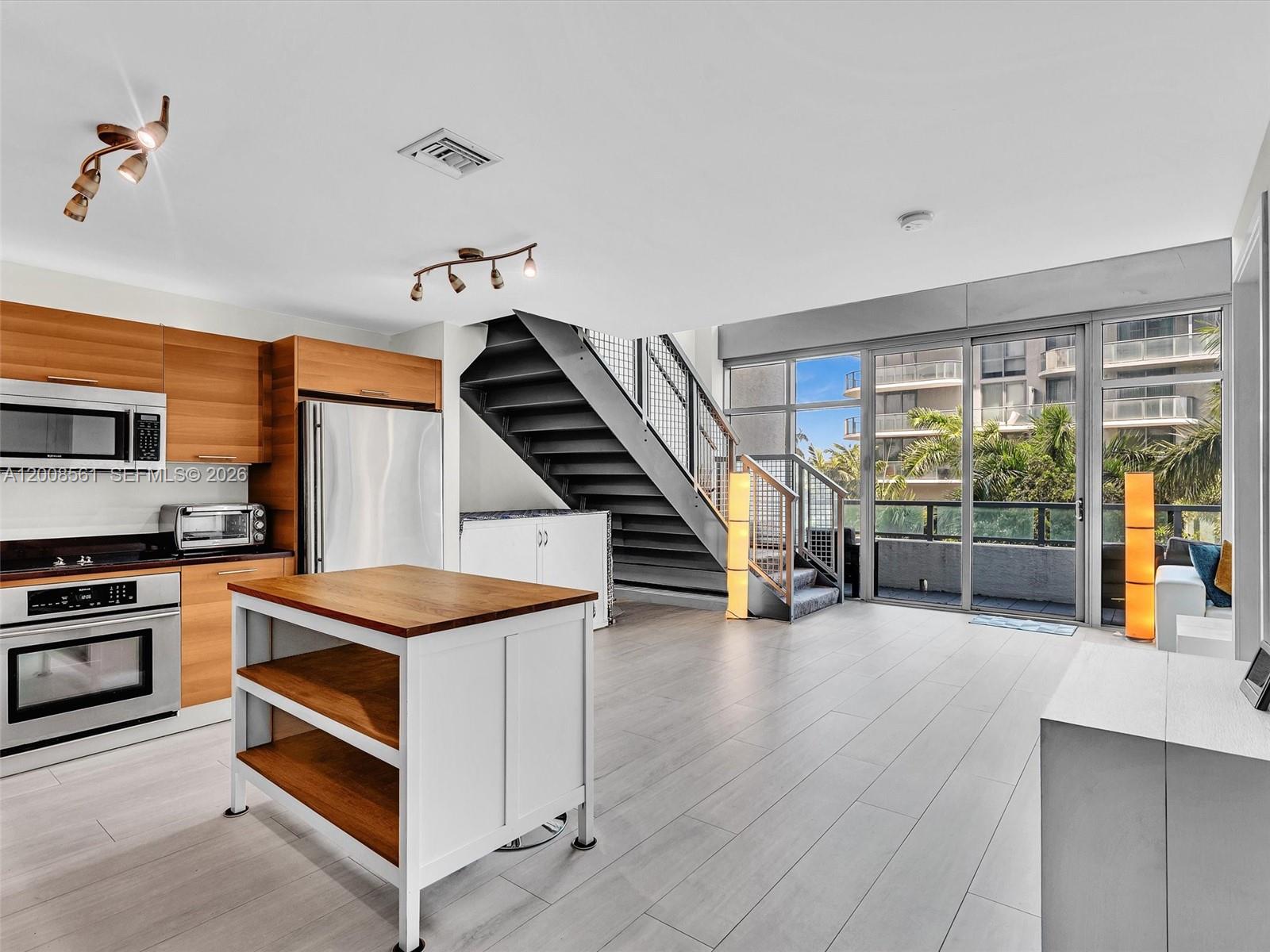 A modern kitchen and living area features wood cabinetry, a central island, and a staircase — 3301 NE 1st Ave # M0306, Miami FL 33137, MIAMI, FL