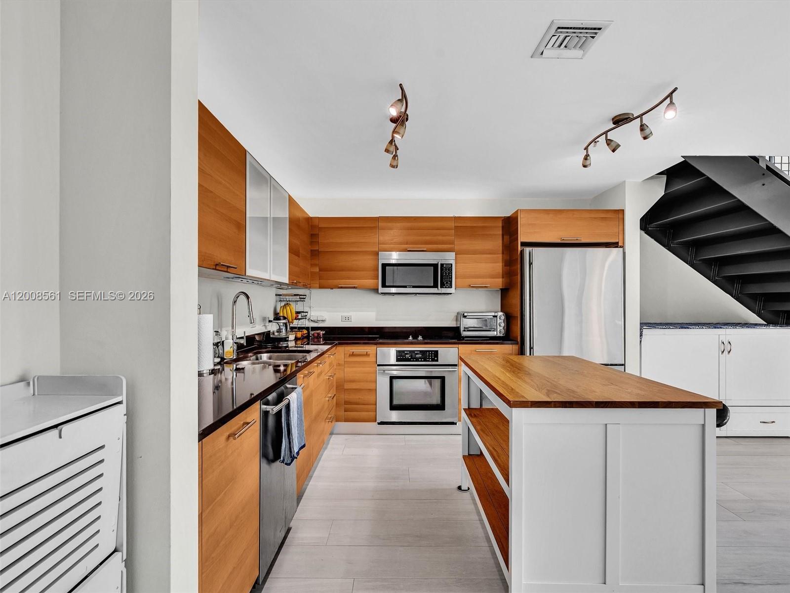 A kitchen features wood cabinets, stainless steel appliances, a center island, and a staircase — 3301 NE 1st Ave # M0306, Miami FL 33137, MIAMI, FL