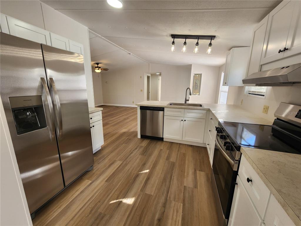 A kitchen with white cabinets, stainless steel appliances, and wood-look flooring opens to a living area — 7351 NW 170TH STREET, TRENTON, FL