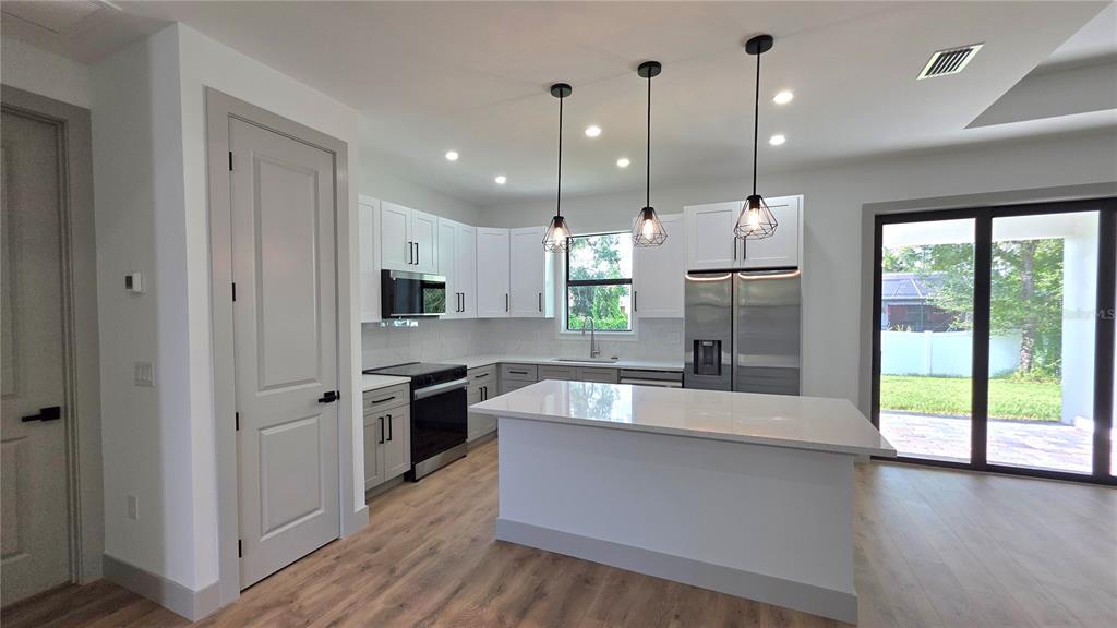 A modern kitchen features white cabinets, stainless steel appliances, a center island, and wood flooring — 4802 SUNBURST AVENUE, NORTH PORT, FL