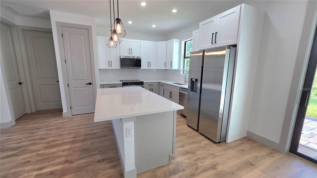 A modern kitchen features white cabinets, stainless steel appliances, a quartz island, and wood-look flooring — 4802 SUNBURST AVENUE, NORTH PORT, FL