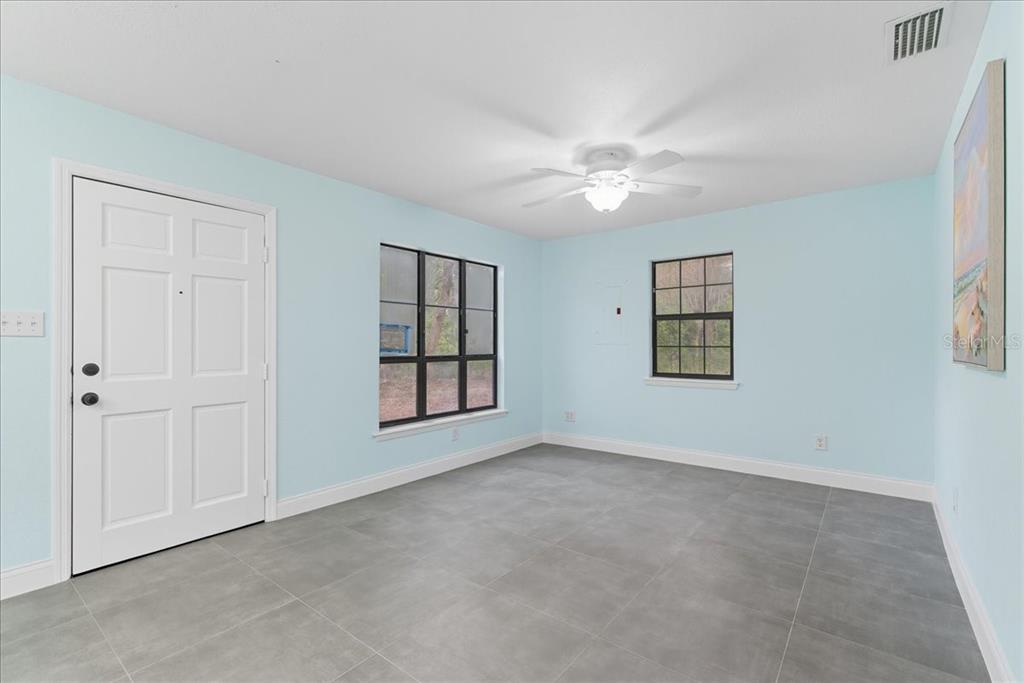 A room with light blue walls, gray tile flooring, a ceiling fan, and two windows — 21445 SE 64TH AVENUE, HAWTHORNE, FL