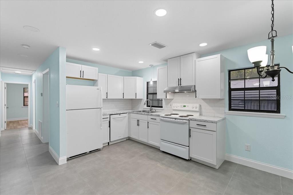 A kitchen features white cabinets, white appliances, light blue walls, and gray tile flooring — 21445 SE 64TH AVENUE, HAWTHORNE, FL