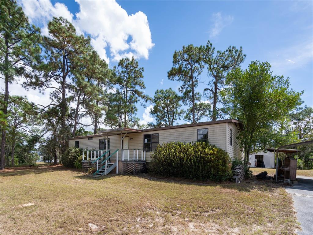 A single-story manufactured home with a wooden deck sits on a grassy lot with trees — 4982 W WOODLAWN STREET, DUNNELLON, FL