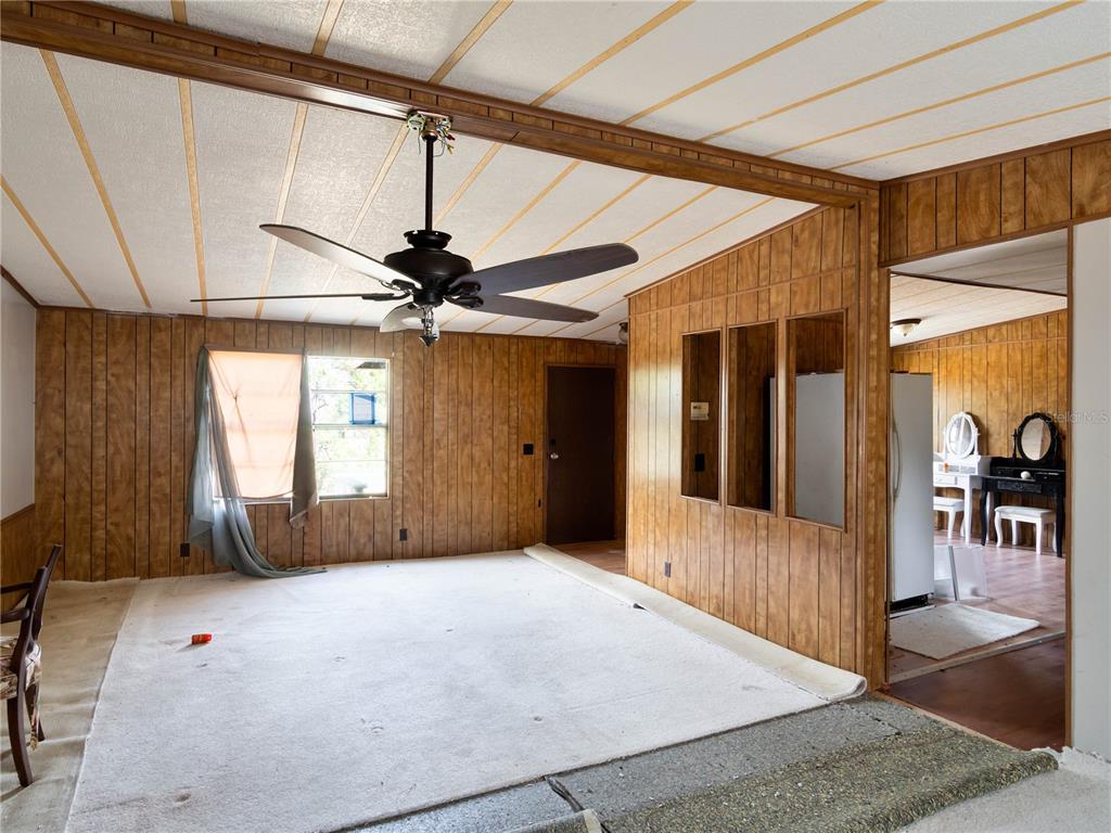 A room with wood-paneled walls, a ceiling fan, and partially removed carpet flooring — 4982 W WOODLAWN STREET, DUNNELLON, FL