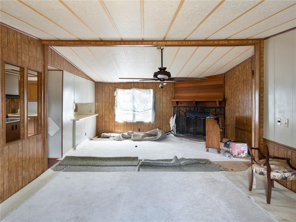 A living room features wood-paneled walls, a stone fireplace, a ceiling fan, and worn carpeting — 4982 W WOODLAWN STREET, DUNNELLON, FL