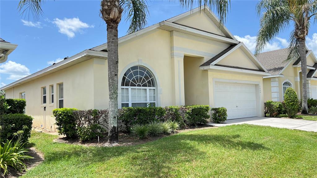 A yellow single-story house with a two-car garage, arched window, and palm trees — 1934 MORNING STAR DRIVE, CLERMONT, FL