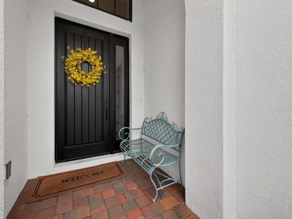 A black front door with a yellow wreath sits beside a blue metal bench — 268 HAMPTON LOOP, DAVENPORT, FL