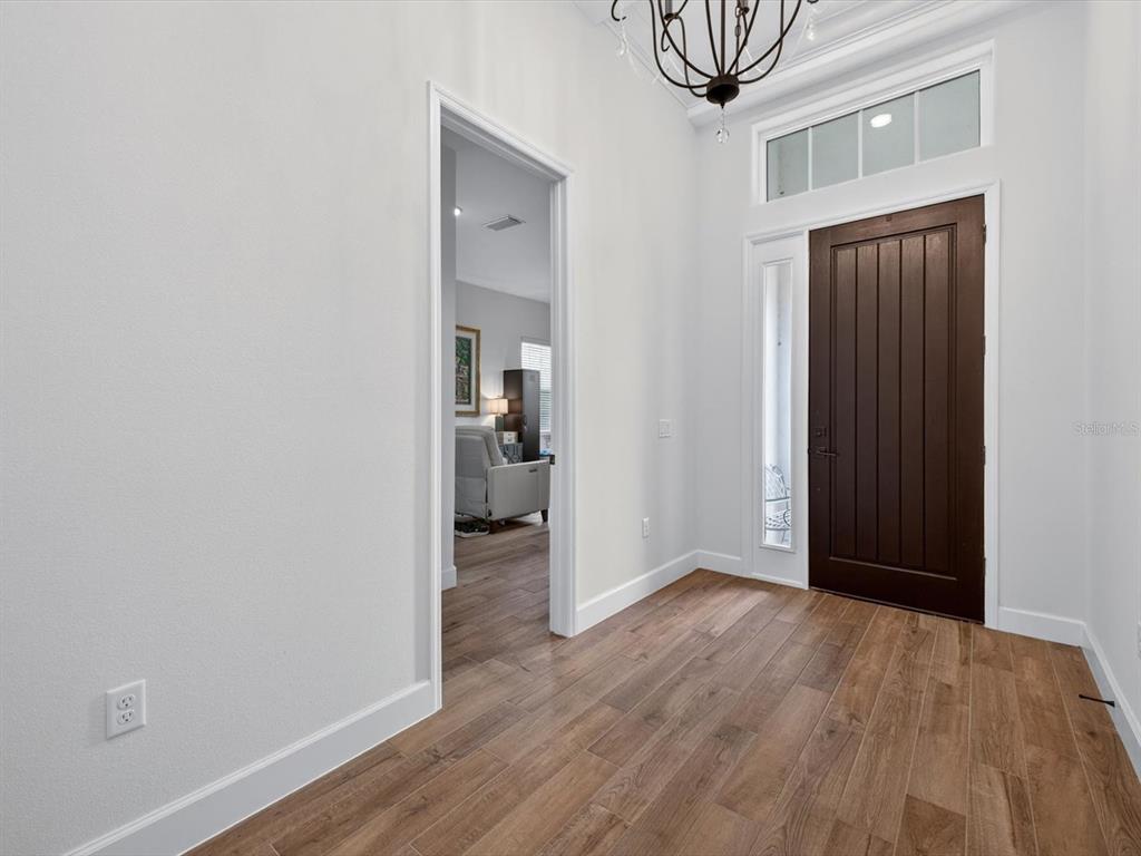 An entryway features a dark wood front door, light wood-look flooring, and a chandelier — 268 HAMPTON LOOP, DAVENPORT, FL